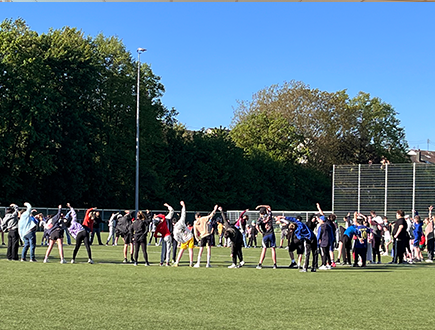 Schülerinnen und Schüler führen gemeinsam Kreisübungen auf dem Sportplatz im Rahmen der Bundesjugendspiele durch.