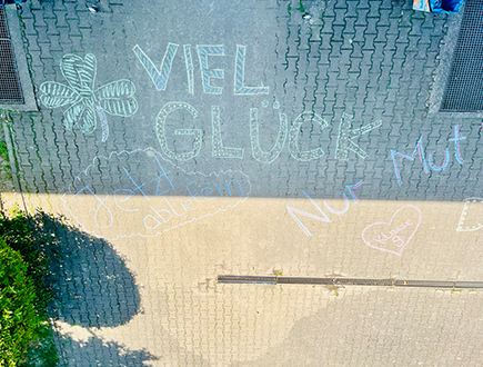 Mit Kreide geschriebene Glückwünsche „Viel Glück“ auf dem Schulhof zur Motivation der Schülerinnen und Schüler vor den Abschlussprüfungen.