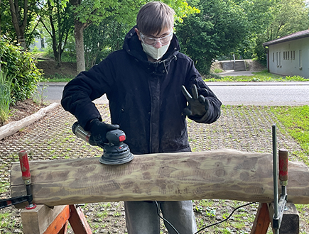 Schüler der Pestalozzischule schleift einen Holzbalken für die Neugestaltung des Eingangsbereichs